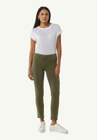 Witte T-shirt met korte mouwen gecombineerd met olijfgroene strakke broek en witte sneakers. De stof lijkt glad met standaard naden en zonder patronen.