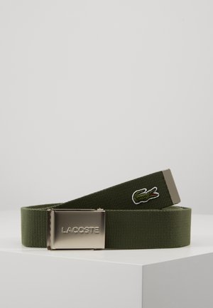 Oliivinvihreä kangasvyö hopeisella metallisoljella, johon on painettu "LACOSTE"-teksti ja vyön päässä kirjottu vihreä krokotiililogo.
