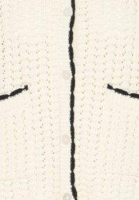 Cardigan en maille crème avec des accents de bordure noire le long de la ligne de boutons et des poches, présentant un motif texturé à mailles ouvertes.