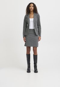 Grau meliertes Blazer- und Rock-Set mit maßgeschneiderter Passform, strukturiertem Stoff, einem weißen eng anliegenden Oberteil und knielangen schwarzen Lederstiefeln.