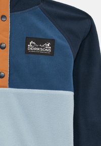 Giacca in fleece blu e blu navy con pannello azzurro chiaro, striscia di bottoni marroni e patch del logo Didriksons con montagne e testo sul petto.