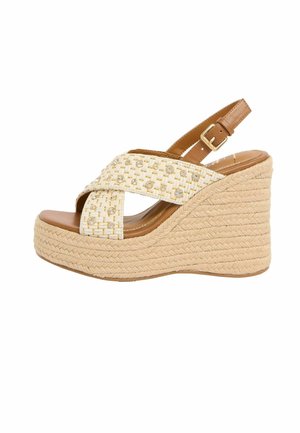 Beżowy sandał na koturnie z plecioną podeszwą na platformie, skrzyżowane plecione paski ozdobione małymi ćwiekami oraz regulowany pasek wokół kostki z złotą klamrą.
