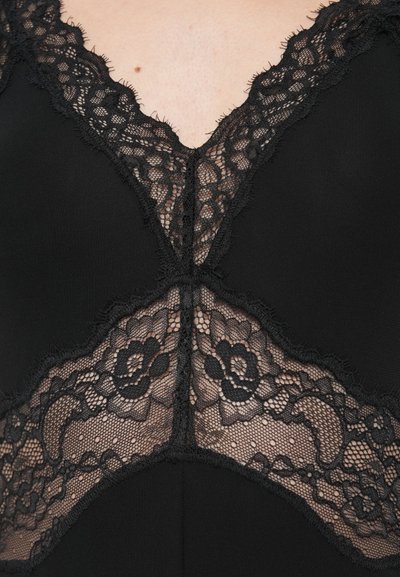 Czarny strój z dekoltem w kształcie litery V ozdobionym kwiatową koronką i postrzępionymi krawędziami, połączony z gładką czarną tkaniną.