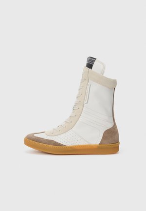 Sneaker alta caratterizzata da una combinazione di pelle bianca liscia e suede beige, dettagli per perforazione, lacci beige e suola in gomma.