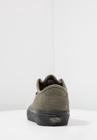 Boty ke tenisu z olivově zelené semiše s kulatou špičkou, černou plochou gumovou podešví a logem na patě. Hladká textura a minimalistický design.