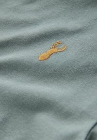 Light blue fabric with a soft texture features a golden embroidered lobster design, positioned near the center.