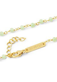 Collana a catena color oro con perline sfaccettate di un verde chiaro. Include un gancio a moschettone e un'etichetta incisa con la scritta "SINGULARU".