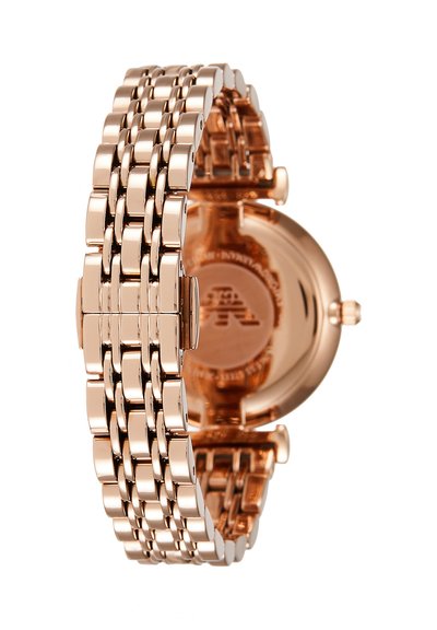 Bracelet de montre à maillons en métal or rose avec une boucle fermée et un fond de boîtier rond partiellement visible.