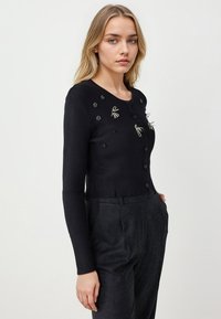 Cardigan noir à côtes avec des manches longues, un col rond et une fermeture à boutons. Présente des broderies florales et des accents texturés à l'avant.
