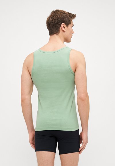 Débardeur vert menthe en tissu doux, avec un col rond et des bretelles larges. Porté avec un short noir.