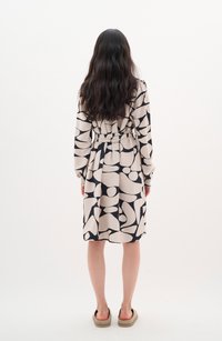 Long-sleeve, belted dress in cream with a black abstract pattern. Soft, textured fabric, knee-length, with a rounded hem and cuffed sleeves.