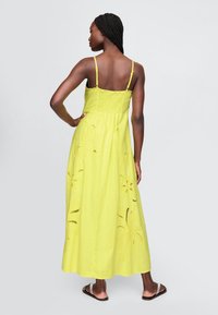 Gul maxikjole med tynde stropper, smocket overdelsstykke og blomsterudskæringsdetaljer i kanten. Letvægtsstof for en afslappet pasform.