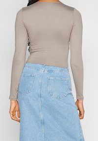 Långärmad, taupe-färgad, åtsittande topp i ett mjukt material, kombinerad med en ljusblå denimkjol med bakfickor och rak skärning.