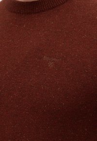 Gros plan d’un pull marron tricoté avec le logo Barbour brodé sur la poitrine et un col rond côtelé.