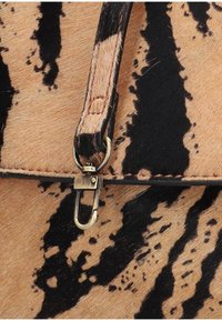 Dettaglio di una borsa a tracolla marrone e nera con motivo, caratterizzata da una chiusura con tono dorato, superficie testurizzata, tracolla in pelle e cuciture a contrasto.