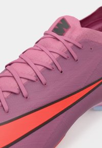 Primo piano di una scarpa sportiva rosa con lacci coordinati e una swoosh Nike rosso-arancio sul lato, che mostra la trama del tessuto e il logo sulla linguetta.