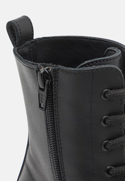 Svart läderstövel med sidokedja, rund tå, strukturerad yta och kontrasterande snören med metalöglor.
