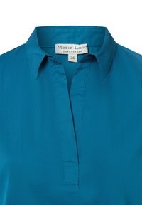 Blusa teal con colletto, dotata di una patta e dettagli di cucitura minimi. Realizzata in tessuto morbido, etichetta Marie Lund, taglia 36.