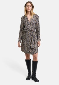Rochie înfășurată cu model floral în nuanțe de bleumarin și aur, cu mâneci lungi și centură legată; combinată cu boobere de piele neagră până la genunchi.