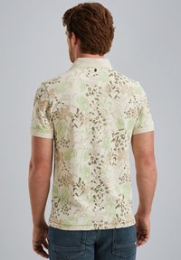 Polo in crema con un motivo floreale verde e marrone. Maniche corte, colletto a coste e un piccolo dettaglio con bottone sul retro.