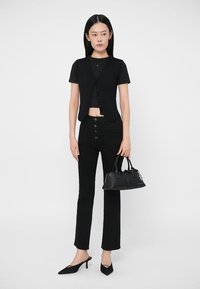 Colete preto canelado por cima de uma camisola preta justa, combinado com calças pretas de perna reta e cintura alta. Acessórios incluem uma pequena mala preta.