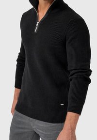 Pull en maille noire avec col zippé, manches longues et accent logo sur le côté. Confectionné en tissu doux et texturé.