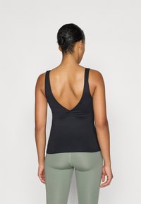 Fekete, ujjatlan tank top mély V-háttal, puha anyagból készült. Világos zöld, magas derekú leggings-szel párosítva, sima textúrával.