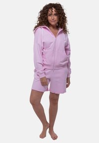 Lichtroze hoodie met ritssluiting en koordjes, gecombineerd met bijpassende roze shorts met een gegolfde zoom, gemaakt van zachte, gestructureerde stof.