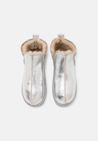 Metallisk sølvfarge slip-on sko med myk beige innvendig, avrundet tå og sydd kant. Har løkke for enkel bruk. Myk tekstur.