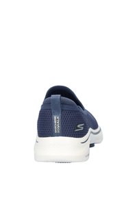 Zapatillas slip-on de color azul marino con parte superior de malla texturizada, paneles elásticos, entresuela blanca y la marca "Skechers GOwalk" en el talón.
