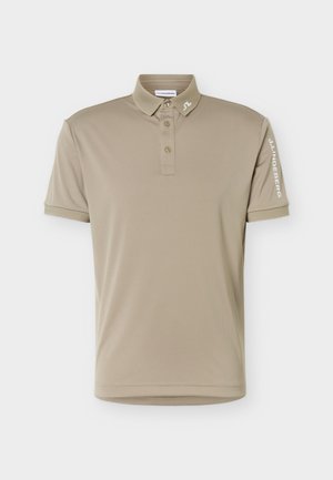 Beige lyhythihainen poolopaita, jossa on kolme nappia, pieni logo kauluksessa ja "J.LINDEBERG" painettuna vasempaan hihaan.
