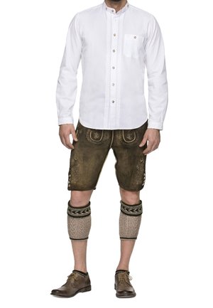 Homme portant une tenue bavaroise traditionnelle comprenant une chemise blanche à boutons, un short en cuir marron jusqu'aux genoux, des guêtres tricotées pour les mollets et des chaussures habillées marron.