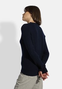 Marineblaues geripptes Sweatshirt mit hohem Kragen, langen Ärmeln und strukturierter Strickart. Die Rückansicht zeigt die figurbetonte Form und die lässige Silhouette.