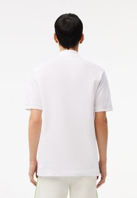 Camisa polo blanca de manga corta, con collar clásico y una textura suave. Diseño simple sin patrones o acentos visibles.