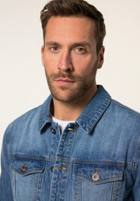 Blå denimjacka med två bröstfickor, grå knappar och orange sömmar. Styld med en vit skjorta under. Strukturerad krage.