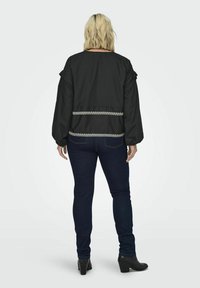Czarna kurtka bomberka z dopasowanym pasem, z bufiastymi rękawami i białą haftowaną zygzakiem na dole. Połączona z ciemnymi dżinsami.