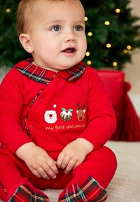 Rød babybody med ternet krave, prydet med broderede julemønstre: julemand, juleskinke, rensdyr og teksten "min første jul".