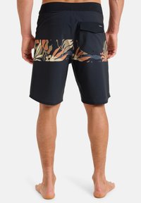 Bañador negro con un diseño texturizado, que presenta un colorido patrón floral en los bolsillos traseros y un bolsillo con solapa a la derecha.