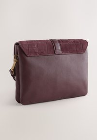 Maroon leather clutch with a textured suede flap, rectangular shape, and a magnetic closure. Features a single gold-toned hardware accent.