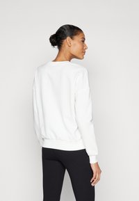 Sweatshirt blanc à col rond et avec des poignets et un ourlet côtelés. Texture lisse, coupe décontractée. Porté avec des leggings noirs.