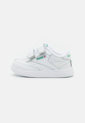 Baskets en cuir blanc avec des bandes Velcro, langue en mesh et accents de logo vert subtils. Design à profil bas avec un bout perforé pour la respirabilité.