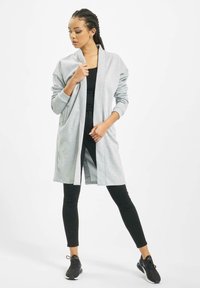 Cardigan lung gri cu guler de tip șal, deschis în față, cu umeri lăsați și manșete cu model, purtat peste un top negru și colanți.