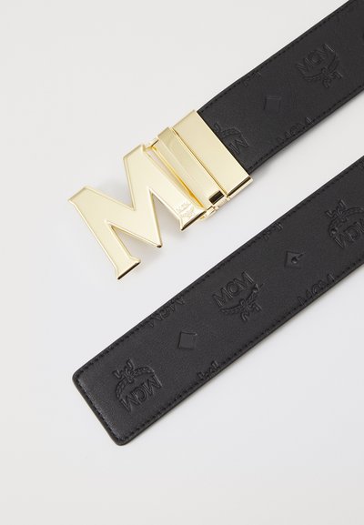 Schwarzer Ledergürtel mit einer glänzenden goldenen Monogrammschnalle, auf der die Buchstaben "MCM" stehen. Der Gürtel ist mit einem Logomuster geprägt.