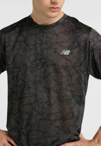 Black short-sleeve athletic t-shirt featuring a patterned texture, round neckline, and a reflective New Balance logo on the left chest.