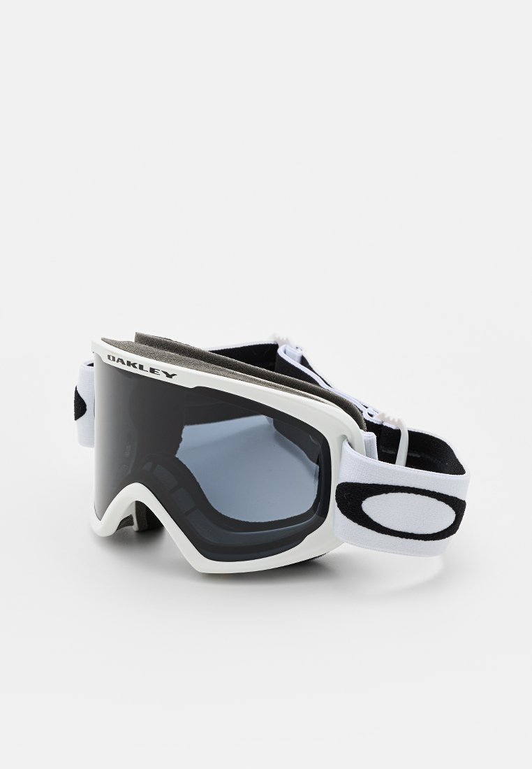 Gafas de esquí Oakley con un marco de plástico blanco, lentes oscuros y una correa ajustable en negro y blanco. Acolchado suave a lo largo del borde interior.