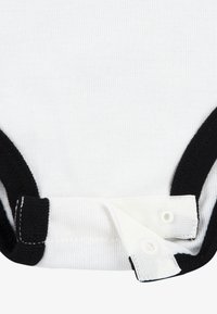 Body blanc avec bordures côtelées noires au niveau du cou et des ouvertures des jambes. Présente une fermeture à pression blanche. Tissu en coton doux et texturé.