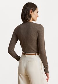 Bruine lange mouwen gebreide trui met een ronde halslijn, gecombineerd met witte hoge taille broek. Soepele textuur, aansluitende silhouet, minimalistisch ontwerp.