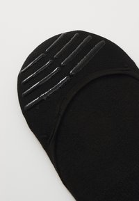 Calcetín negro con patrón de agarre de goma en la suela. Fabricado en tejido suave, con una textura lisa y un diseño sin costuras.