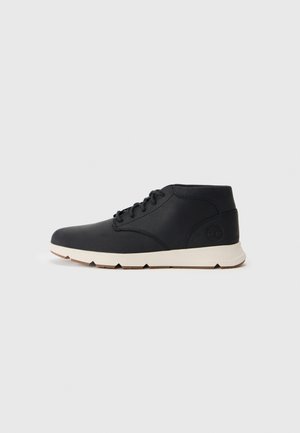 Schwarzer Leder-Mid-Top-Schnürschuh mit weißer Sohle und geprägtem Logo an der Ferse, isoliert auf hellgrauem Hintergrund.