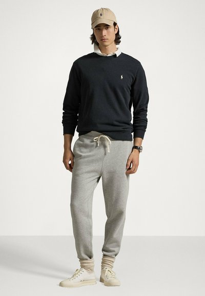 Maglione blu scuro, pantaloni della tuta grigi con coulisse, cappellino beige con logo e sneakers beige chiaro. Abbigliamento sportivo semplice e casual.